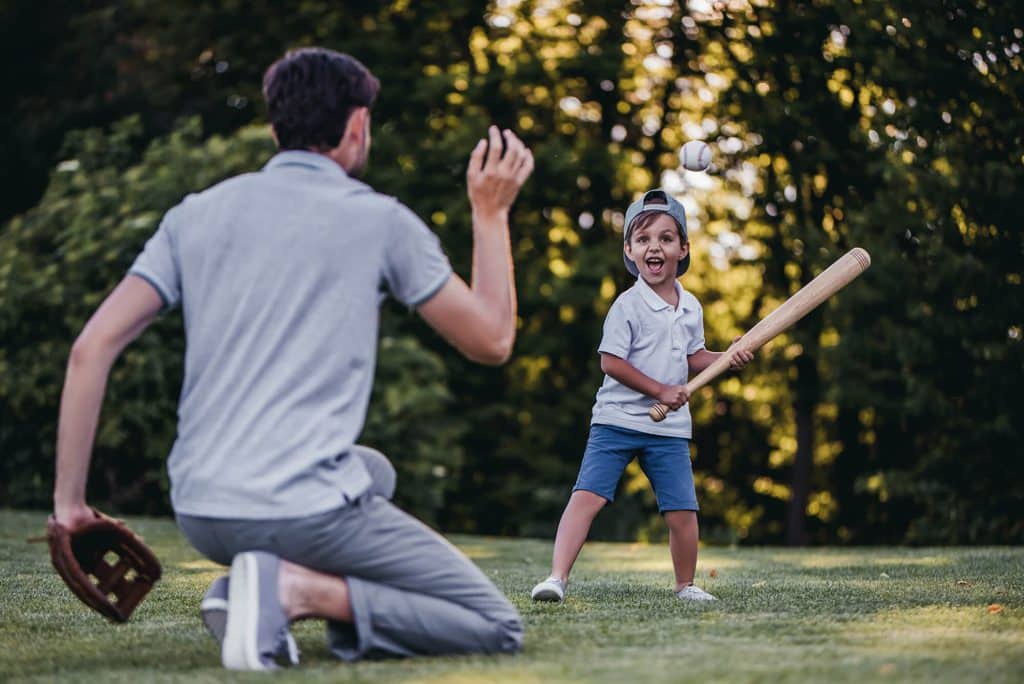 boy with a bat and a man tossing a baseball at Meridian Homes rentals indianapolis at mccordsville.