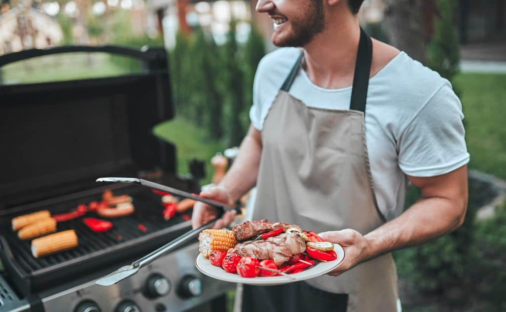 man grilling food with an apron on and tongs in his hand at Meridian homes Mccordsville rentals indianapolis